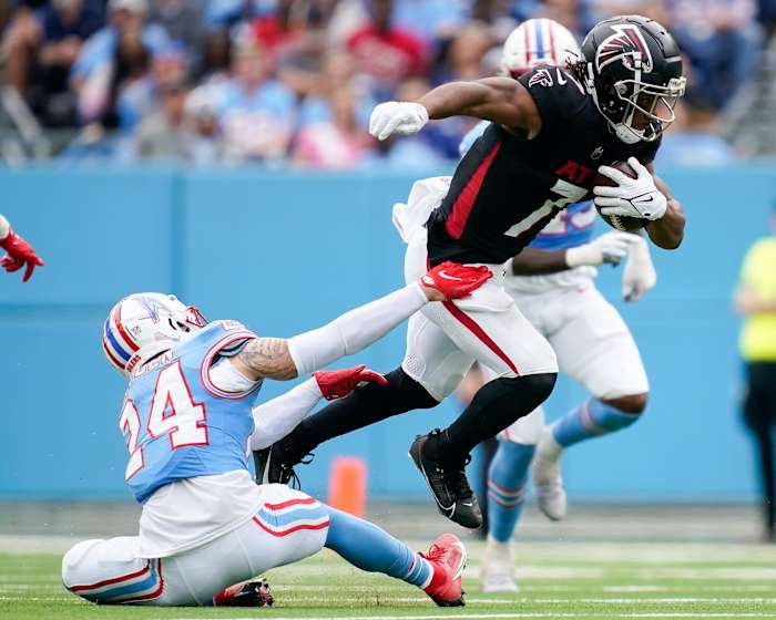 Bijan Robinson leaps while holding the ball as a Titans defender tries to grab his legs